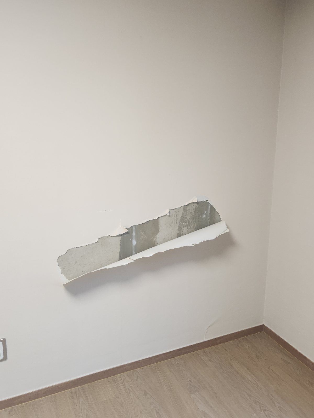방 벽 가운데 벽지가 가로로 길게 뜯겨 속 벽면이 드러난 상태 - 작업 전